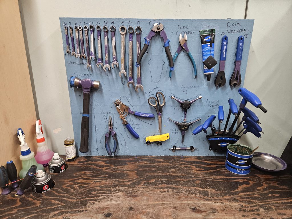 individual workstation. Blue board. outline of tools with black sharpie. Tools small sections with purple. there are wrenches, cutters, allen keys, lubricants and oils.